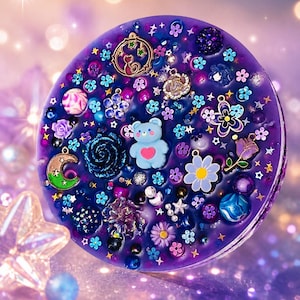May include: A circular purple resin disc embedded with various charms including a light blue bear with a pink heart, a crescent moon, a flower with a yellow centre, a cat silhouette, and numerous small colourful beads, stars, and floral accents.
