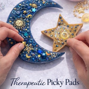 K&ouml;nnte beinhalten: Ein blauer Halbmond und ein goldfarbenes sternf&ouml;rmiges Objekt, beide mit Verzierungen zum Thema Himmel dekoriert. Der Mond und der Stern werden von H&auml;nden gehalten. Der Text "Therapeutic Picky Pads" ist sichtbar.