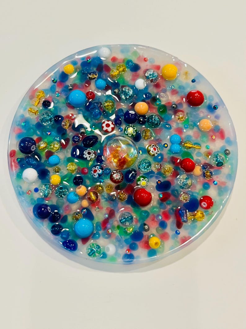 Peut inclure: Une &oelig;uvre d'art en r&eacute;sine ronde et transparente, remplie de perles et d'ornements color&eacute;s. La pi&egrave;ce pr&eacute;sente une vari&eacute;t&eacute; de couleurs, dont le bleu, le rouge, le jaune et l'orange. Les perles sont de tailles et de formes vari&eacute;es, cr&eacute;ant un design textur&eacute; et vibrant.