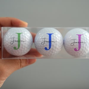Peut inclure: Trois balles de golf blanches avec le nom "Jason" et la lettre "J" en vert, bleu et violet.