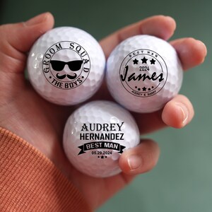 May include: Three white golf balls with black text. One ball says "Groom Squad The Boys" with sunglasses and a mustache. Another says "Best Man James 2024". The third says "Audrey Hernandez Best Man 05.29.2024".