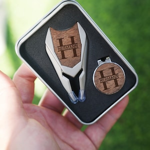 以下が含まれることがあります： 黒いギフトボックスに入った、木製のハンドルに「HERMANN」と刻まれた銀製のゴルフツールセットです。