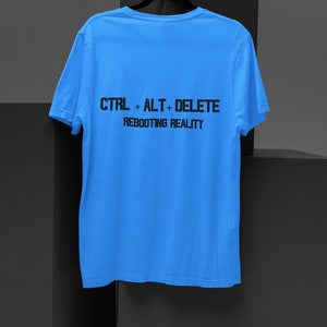 Può includere: Una maglietta blu chiaro con la scritta "CTRL + ALT + DELETE REBOOTING REALITY" stampata sul retro.