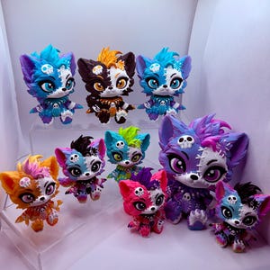May include: A collection of nine stylized animal figurines featuring vibrant colors, stitched patterns, and small skull accents on their heads and bodies. The figures display various color combinations including blue, orange, pink, and purple.