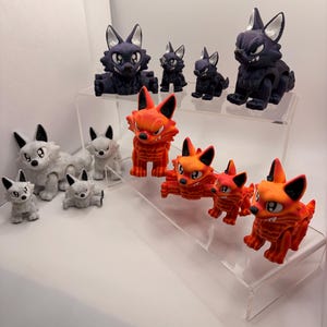 Puede incluir: Una colección de figuras de zorro estilizadas en varios tamaños y colores. Las figuras están dispuestas en estantes transparentes. Los zorros son principalmente negros, blancos y naranjas, con detalles y una expresión enfadada.
