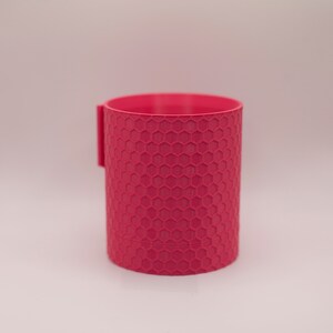 May include: A pink cylindrical cup with a honeycomb pattern.