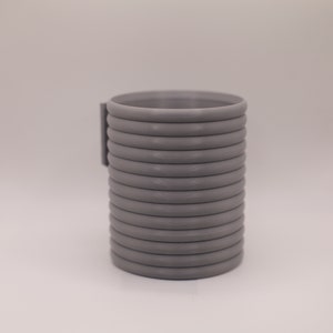 May include: A cylindrical, gray object with a series of horizontal, rounded ridges. A rectangular piece is attached to the side. The object appears to be made of a solid material and is set against a plain background.