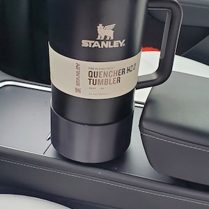 Puede incluir: Un vaso Stanley Quencher H2.0 negro con una tapa negra y un asa negra. El vaso tiene una etiqueta blanca que dice "The Flowstate Quencher H2.0 Tumbler 64 oz | 1.9 L All Day Hydration".