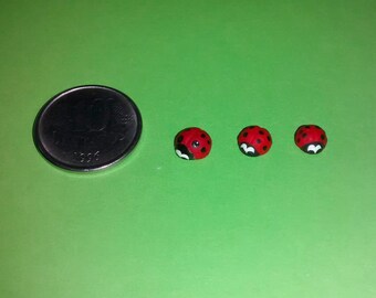 May include: Three small red and black ladybug figurines on a green surface.