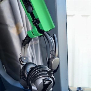 May include: A green headset holder with a black headset hanging from it. The headset is a Sennheiser HME 20 model.