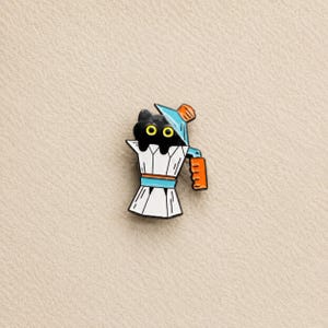May include: A metal enamel pin shaped like a white moka pot coffee maker with a black cat head peeking out from the top. The design features a light blue lid and handle, an orange side handle, and black outlines on a white body with yellow eyes.