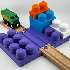 Könnte beinhalten: Ein farbenfrohes Spielzeug-Zugset mit einem grünen Zug, Holzschienen und bunten Bausteinen in Lila, Blau, Orange und Weiß. Das Set ist für fantasievolles Spielen und Konstruieren konzipiert, mit Maßen in cm.