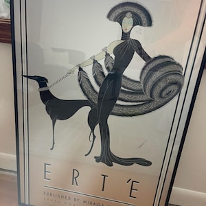 May include: A framed art print featuring a stylized figure in a black gown with a large feathered wrap and headpiece, holding a leash attached to a black greyhound. The text ERTE, PUBLISHED BY MIRAGE EDITIONS, SANTA MONICA, CALIFORNIA is visible.
