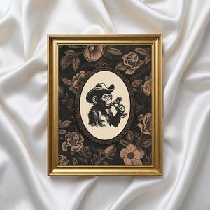 May include: A framed art print featuring a black and white illustration of a monkey wearing a cowboy hat and holding a cocktail. The monkey is set within an oval frame against a floral background in black and tan. The frame is gold.