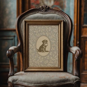 Puede incluir: Un grabado enmarcado con un perro marr&oacute;n sosteniendo un rollo de papel, sobre un fondo floral beige. El grabado est&aacute; en un marco dorado y descansa sobre una silla vintage tapizada con marco de madera.