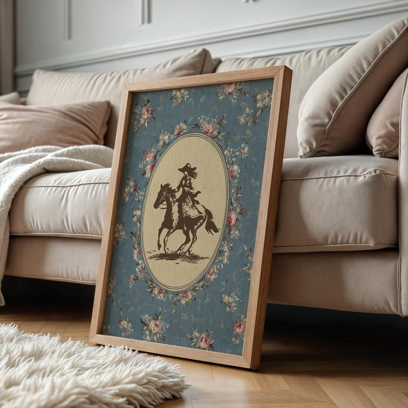 May include: A framed print featuring a vintage illustration of a person riding a horse. The artwork is set against a blue floral background with a light brown oval frame. The wooden frame adds a rustic touch.