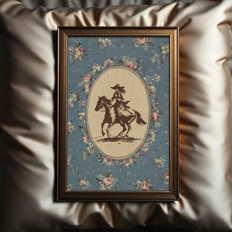 May include: Framed artwork featuring a sepia-toned illustration of a person riding a horse. The image is set within an oval frame, surrounded by a floral wreath on a blue background. The frame is a dark brown color.