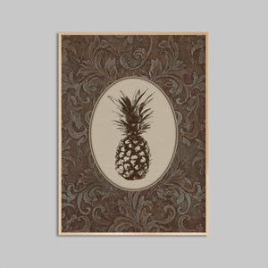 May include: A framed print featuring a detailed illustration of a pineapple within an oval frame. The pineapple is rendered in a sepia tone, set against a beige background. The frame is surrounded by a dark brown and gray floral pattern.