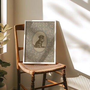 Puede incluir: Una impresi&oacute;n enmarcada con una ilustraci&oacute;n en sepia de un perro sosteniendo un rollo de papel. El perro est&aacute; dentro de un marco ovalado, sobre un fondo con estampado floral. La impresi&oacute;n se exhibe en una silla de madera con asiento tejido.