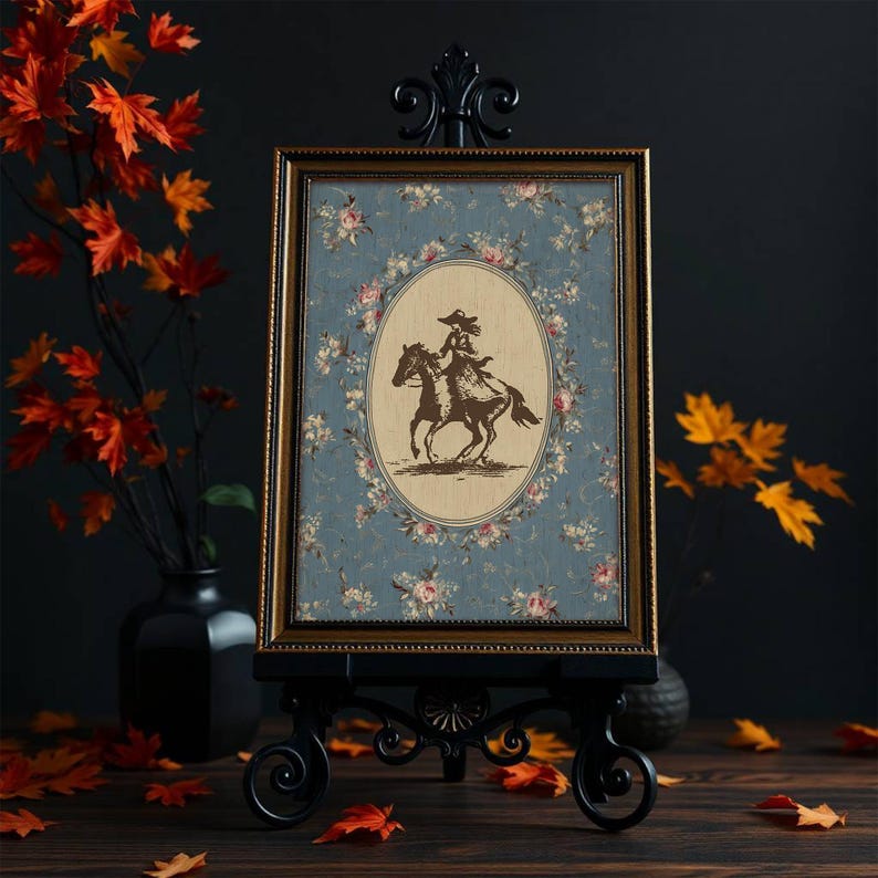 May include: A framed print featuring a sepia-toned illustration of a person riding a horse, set against a floral patterned background. The frame is gold, and the print is displayed on a black easel. The overall aesthetic is vintage and decorative.