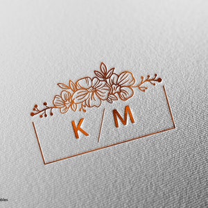 May include: A copper-colored monogram with the initials K/M surrounded by a floral design in a square frame.