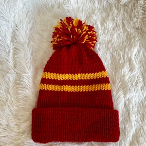 Peut inclure: Bonnet en tricot rouge avec un pompon jaune et deux rayures jaunes.