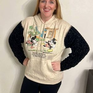 May include: A beige hoodie with black sleeves featuring a Mickey Mouse and Minnie Mouse graphic. The graphic shows Mickey and Minnie walking with the text "Mickey & Minnie Have Places To Go & Friends To See".