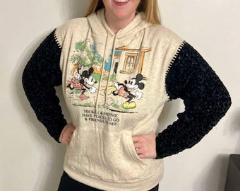 May include: A beige hoodie with black sleeves featuring a Mickey Mouse and Minnie Mouse graphic. The graphic shows Mickey and Minnie walking with the text "Mickey & Minnie Have Places To Go & Friends To See".
