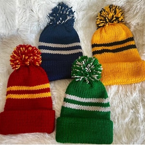 Puede incluir: Cuatro gorros de punto con pompones. Los gorros son de color rojo, amarillo, azul y verde. Cada gorro tiene dos rayas blancas.