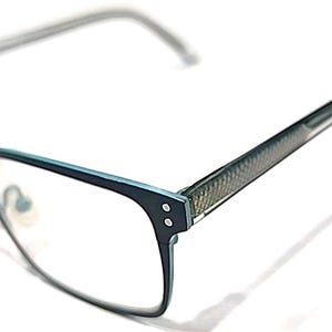 May include: Teal and dark blue eyeglasses featuring a rectangular frame design with two small silver rivets on each side of the front. The temples have a textured, cross-hatched pattern and the nose pads are clear, adjustable, and metallic.