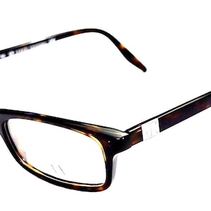 Puede incluir: Gafas con patrón de carey que presentan un diseño de montura rectangular con lentes transparentes. Las varillas están unidas al frente de la montura mediante bisagras de metal plateado y el material tiene un patrón de color marrón oscuro y ámbar.