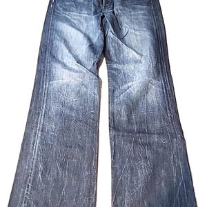 Puede incluir: Vaqueros de mezclilla de lavado oscuro con una apariencia descolorida y texturizada. Los vaqueros tienen bragueta con botones, diseño clásico de cinco bolsillos y pernera ancha. La mezclilla es de peso medio, con sutiles desgastes.