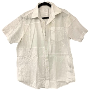 May include: A white short-sleeved button-down shirt featuring a patchwork design with varied textures. The garment includes panels of eyelet lace, floral embroidery, and solid fabric, complete with a standard collar and a single chest pocket.
