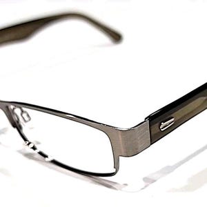 Op de afbeelding: Een rechthoekige bril met een zilverkleurig metalen montuur en donkerbruine veren. De glazen zijn helder en de bril staat tegen een witte achtergrond. Het ontwerp is modern en strak.