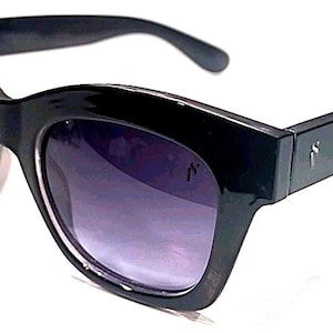 Puede incluir: Gafas de sol negras con montura gruesa y angular y lentes degradadas. Las gafas de sol tienen un pequeño diseño estilizado en las patillas. Las lentes pasan de un morado oscuro a un tono más claro.