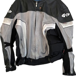 Puede incluir: Chaqueta de moto negra, gris y blanca con el logo "Joe Rocket" en el pecho y el hombro. La chaqueta presenta un diseño de malla, detalles de cuero y cierre de cremallera.
