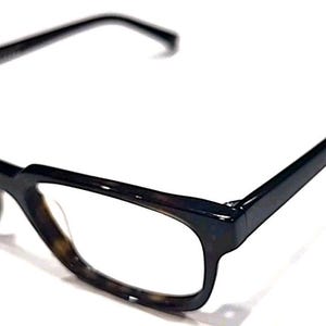 以下が含まれることがあります： ダークブラウンとブラックのべっ甲柄のフレームが特徴の眼鏡。厚みのあるブリッジと外側に伸びる細いテンプルを備えた長方形の形状をしています。レンズは透明でクリアな仕上がりとなっています。