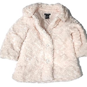 May include: A light pink, faux fur coat with a textured, rose-like pattern. The coat has a rounded collar, three decorative buttons, and three-quarter sleeves. The tag reads "Calvin Klein Jeans".