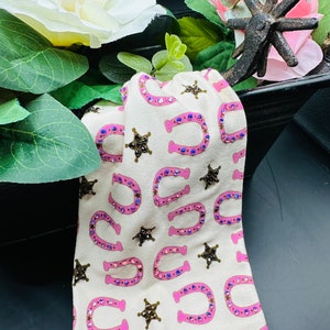 May include: A white fabric headband with a pink and brown horseshoe and star pattern. The pattern is embellished with rhinestones.