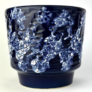 Könnte beinhalten: Dunkelblauer Keramik-Pflanztopf mit einem strukturierten, gesprenkelten Muster in Weiß und Hellblau. Der Topf hat eine breite, zylindrische Form mit einem leicht ausgestellten Boden, geeignet für Innen- oder Außenpflanzen.