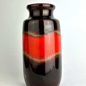 Könnte beinhalten: Eine Keramikvase mit einem dunkelbraunen Sockel, der in ein leuchtend rotes Band in der Mitte übergeht. Das rote Band wird von einem helleren, strukturierten Band begrenzt. Die Oberseite der Vase ist ebenfalls dunkelbraun.
