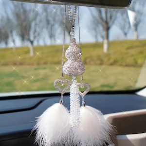 以下が含まれることがあります： リアビューミラーに吊るされた、クリスタル製のひょうたんのデザイン、ハート型のチャーム2つ、白い羽根のタッセルが付いた銀色と白の車のチャームです。
