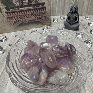 Könnte beinhalten: Eine Schale gefüllt mit irisierenden, getrommelten Amethyststeinen. Die Steine sind hellviolett mit einem schimmernden Finish.