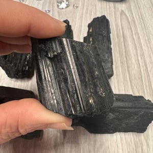 Puede incluir: Cristales de turmalina negra, tambi&eacute;n conocidos como schorl, son un tipo de piedra preciosa conocida por sus propiedades de conexi&oacute;n a tierra y protecci&oacute;n. Estos cristales son en bruto y tienen una textura natural y rugosa.