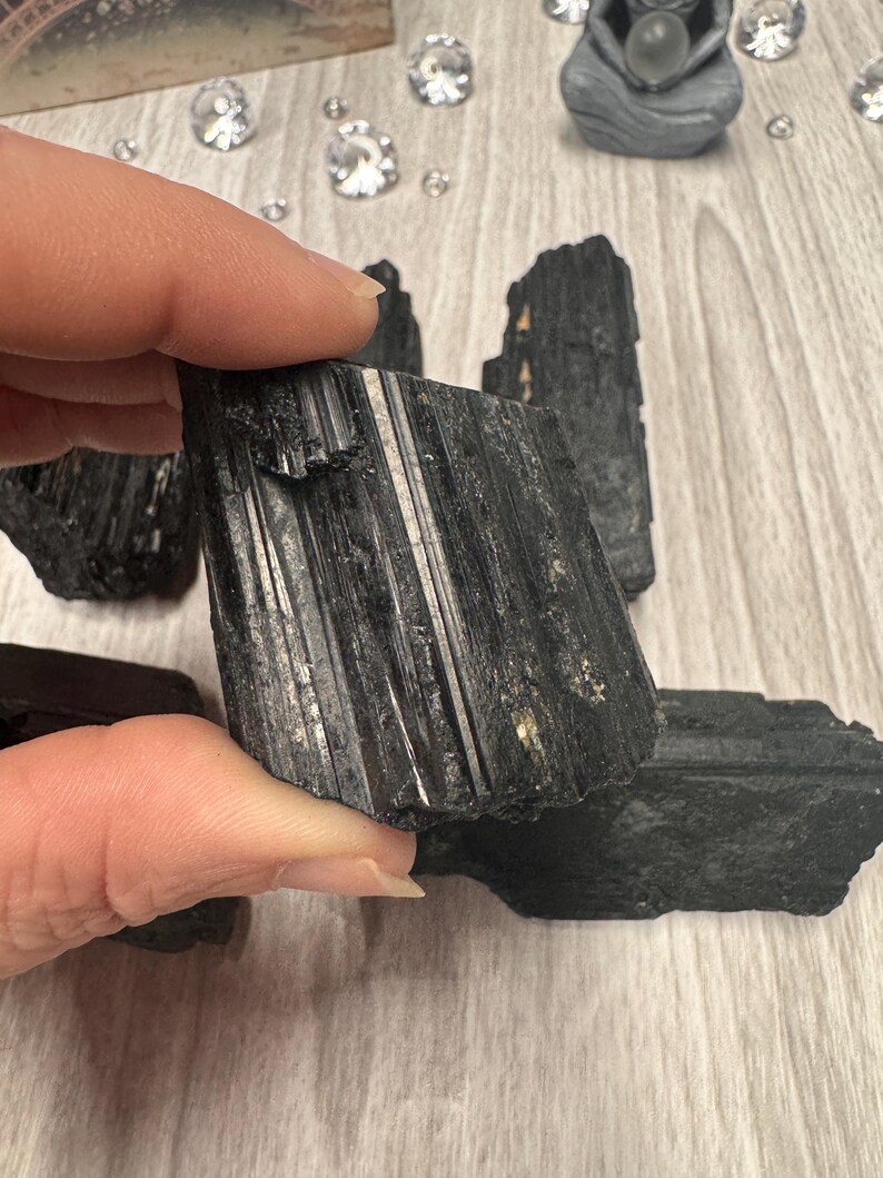 Puede incluir: Cristales de turmalina negra, tambi&eacute;n conocidos como schorl, son un tipo de piedra preciosa conocida por sus propiedades de conexi&oacute;n a tierra y protecci&oacute;n. Estos cristales son en bruto y tienen una textura natural y rugosa.