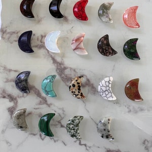Puede incluir: Una colección de 18 piedras pulidas en forma de media luna de varios colores y patrones, incluyendo negro, blanco, rojo, verde y marrón.