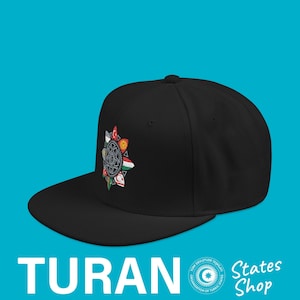 Puede incluir: Gorra negra de ala plana con un emblema colorido con banderas y un diseño central. La palabra "TURAN" está impresa en blanco en la parte inferior, con "States Shop" a la derecha. La gorra tiene un ajuste estructurado.