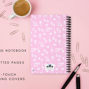 K&ouml;nnte beinhalten: Ein pinkfarbenes, drahtgebundenes Notizbuch mit schwarzer Spiralbindung, verziert mit wei&szlig;en Silhouetten, den Worten "Pole Babe" und "Pole Love". Es hat 140 gepunktete Seiten und Soft-Touch-Beschichtungen. Eine Tasse Kaffee, ein Stift und B&uuml;roklammern sind ebenfalls sichtbar.