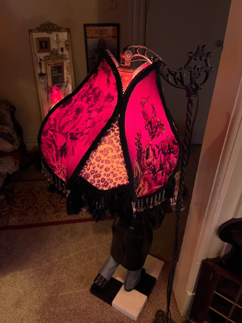 May include: A unique floor lamp with a floral patterned shade in shades of pink and black. The shade is trimmed with black fringe and a leopard print fabric. The lamp has a black metal frame and a checkered base.
