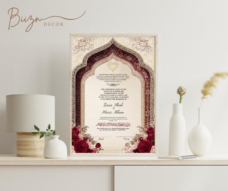 May include: Framed wedding certificate with a decorative arch design in burgundy and cream. The certificate includes the names Zara Shah and Haris Khan, with floral accents. The frame is light-colored, and the overall aesthetic is elegant.